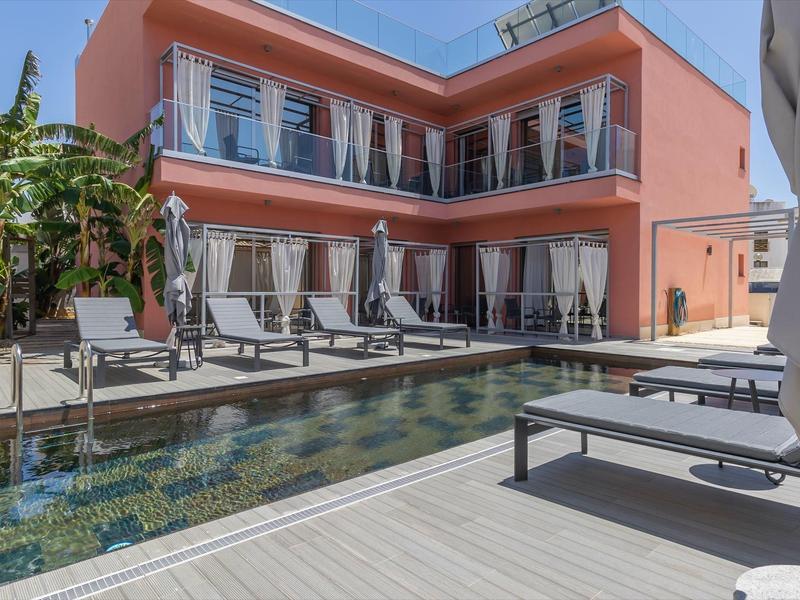 Moderner rosa zwei Stockwerke Bau mit großem schwimmbad und Liegestühlen bei Sonnenschein.