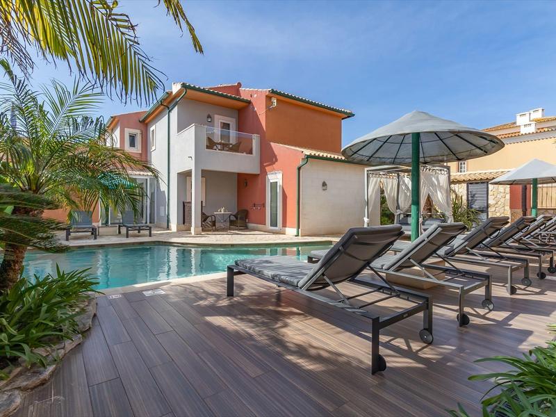 Moderner Poolbereich mit Liegestühlen und Sonnenschirmen vor zweistöckigem Haus bei Sonnenschein.