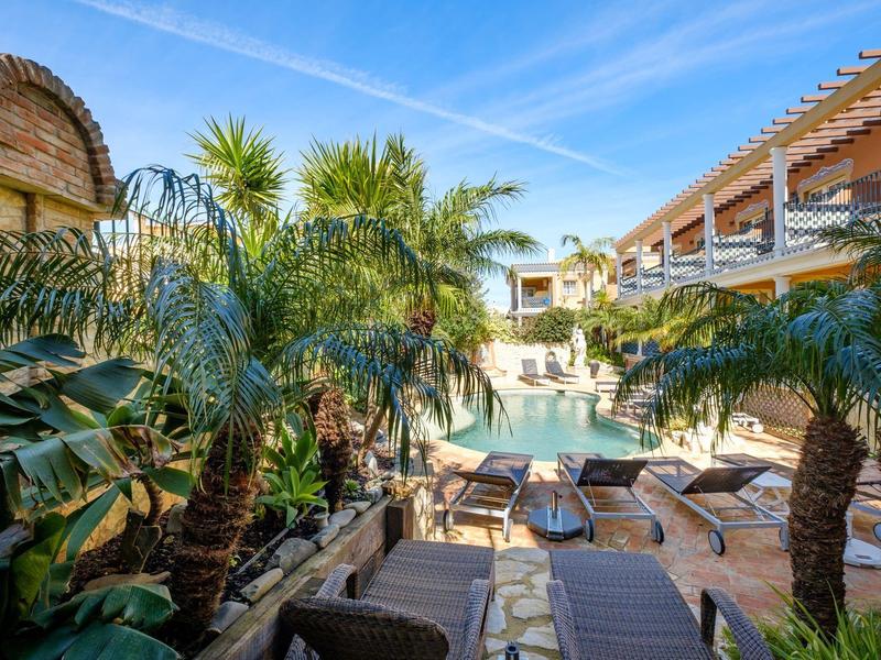 Hotelpool mit Liegestühlen und Palmen unter blauem Himmel an warmem Sonnentag.