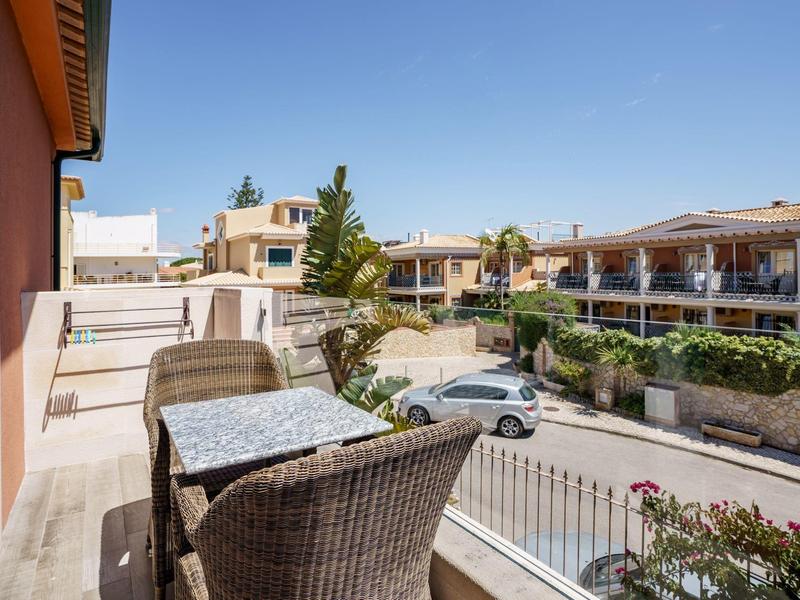 Balkon mit zwei Stühlen und Tisch, Blick auf Parkplätze und mediterrane Gebäude bei Sonnenschein.