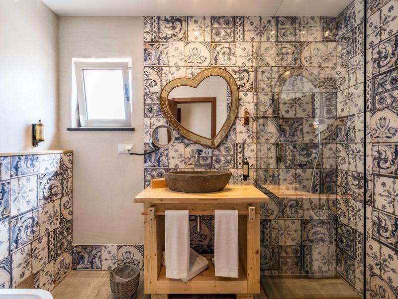 Helles Bad mit blauen Fliesen, Holz-Waschtisch, rundem Spiegel und Glas-Duschwand.