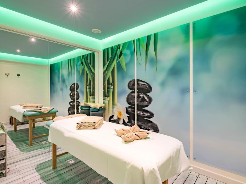 Heller Wellnessraum mit Massageliegen, beruhigenden Steinbildern und grünem Lichtambiente.