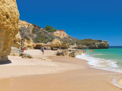 Strand mit goldfarbenem Sand, Felsen und türkisfarbenem Wasser unter klarem blauen Himmel.