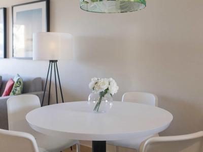 Runder weißer Tisch mit Blumenvasen, umgeben von weißen Stühlen in hellem Wohnzimmer.