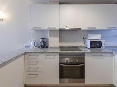 Moderne weiße Küche mit Ofen, Mikrowelle, Kaffeemaschine und Wasserkocher auf grauer Arbeitsplatte.