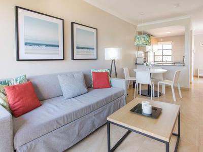 Helles Wohnzimmer mit grauem Sofa, bunten Kissen, modernem Couchtisch und Esstisch im Hintergrund.