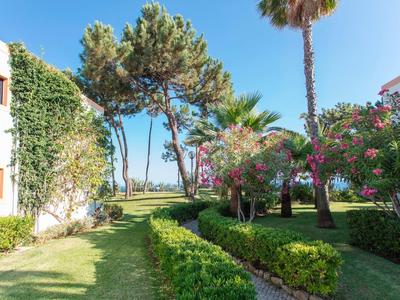 Grüner Garten mit bunten Blumen, Palmen und weißem Gebäude im warmen Sonnenlicht.
