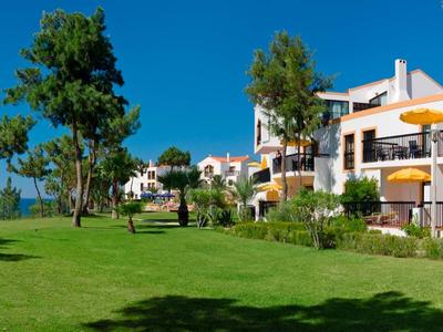 Grüner Rasen mit Palmen vor weißen Häusern unter klarem, blauem Himmel am Meer.