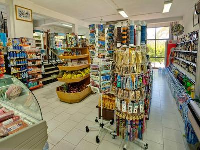 Kleiner Supermarkt mit hellen Regalen, Kühlschränken und einem drehbaren Schlüsselanhänger-Ständer.