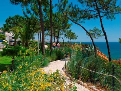 Haus mit weißer Fassade und Garten an felsiger Küste, blauer Himmel und Meer im Hintergrund.
