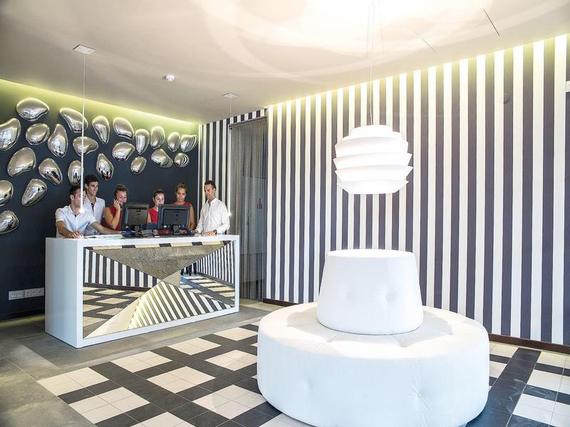 Moderner Empfangsbereich mit gestreiften Wänden, weißem Sitzmöbel und auffälliger Beleuchtung.