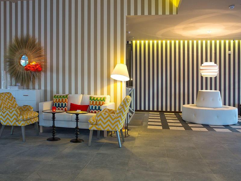 Moderner Wartebereich mit gelben Sesseln, kleinem Tisch, gestreifter Wand und hellem Boden.