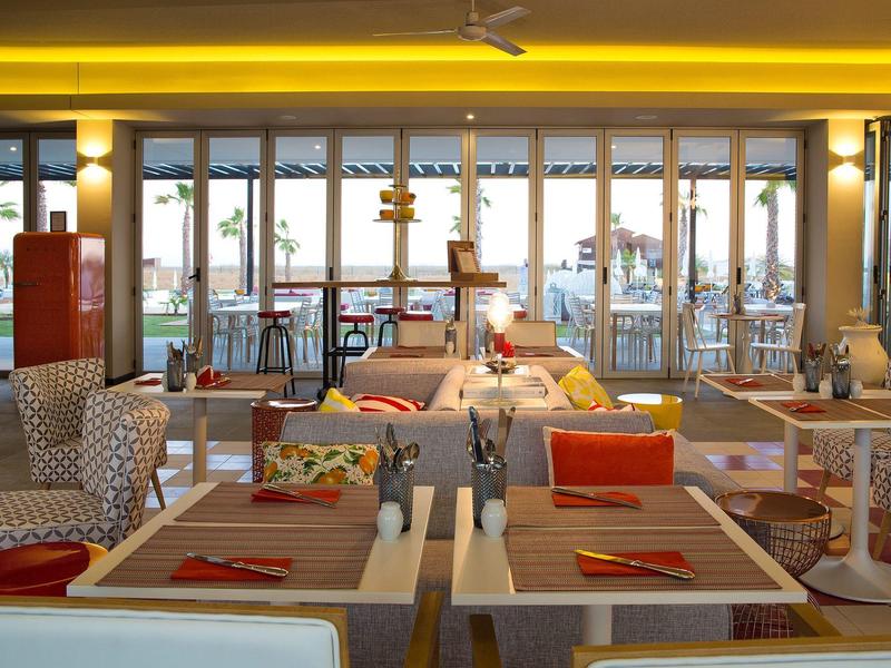 Helles Restaurant mit großen Fenstern, bunten Stühlen und gedeckten Tischen im modernen Stil.