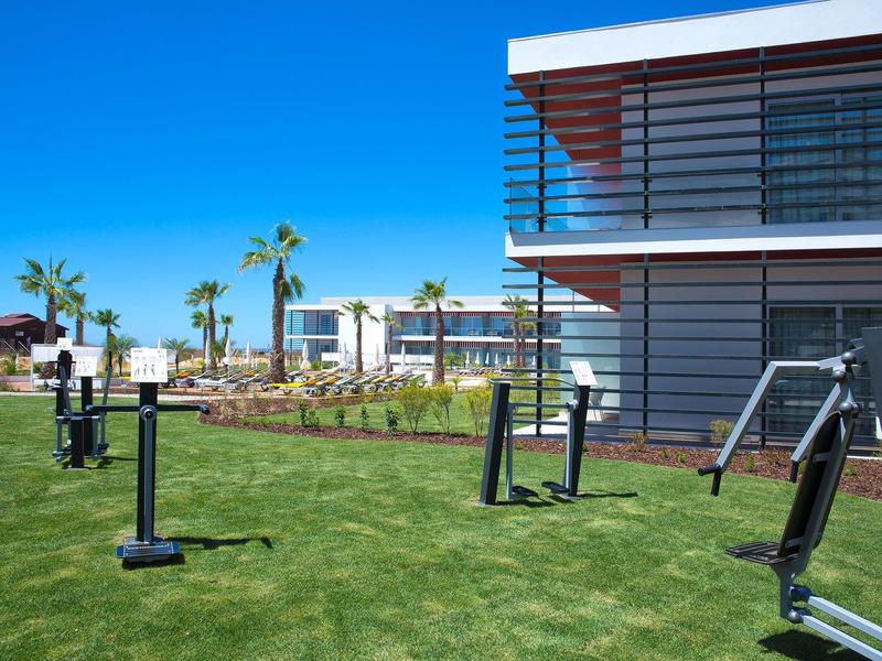 Moderner Außenbereich mit grüner Wiese, Fitnessgeräten und Gebäuden unter klarem blauem Himmel.