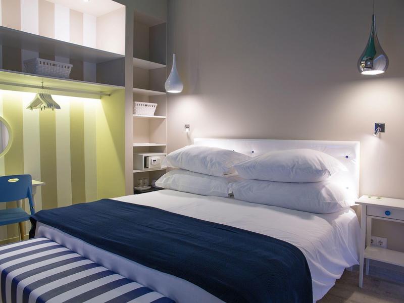 Modernes Schlafzimmer mit weißem Bett, blauen Decken, Regalen und indirekter LED-Beleuchtung.