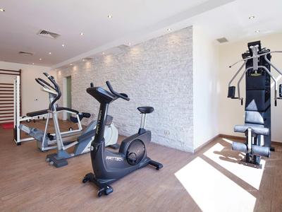 Heller Fitnessraum mit verschiedenen Trainingsgeräten und Holzfußboden.