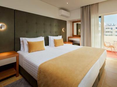 Modernes Schlafzimmer mit großem Bett, hellen Wänden, grünem Kopfteil und Balkon mit Stadtblick.