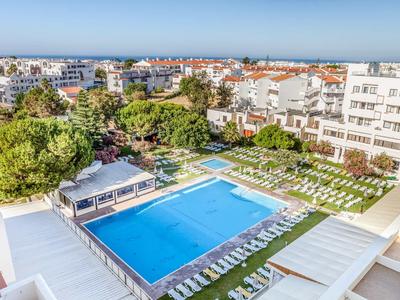 Großer blauer Swimmingpool mit weißen Liegestühlen und grünem Rasen, umgeben von Gebäuden.