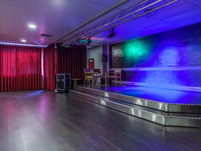 Leerer Veranstaltungsraum mit Bühne, bunten Lichtern und rotem Vorhang
