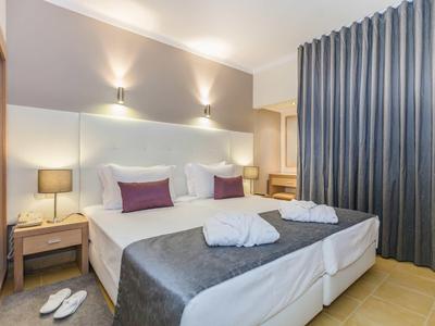 Modernes Schlafzimmer mit Doppelbett, grauem Tagesdecke, Nachttischen und grauen Vorhängen.