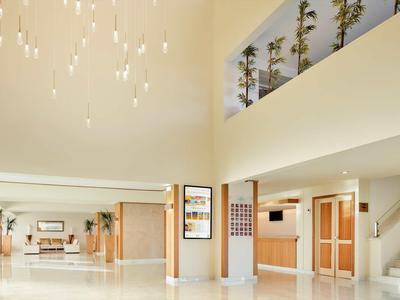 Heller, moderner Hotellobby-Bereich mit Treppe, leuchtenden Kronleuchtern und Sitzgelegenheiten.