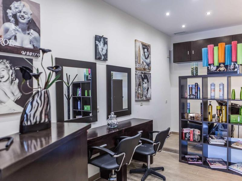 Moderner Friseursalon mit schwarzen Stühlen, Spiegeln, bunten Pflegeprodukten und Marilyn Monroe Bildern.