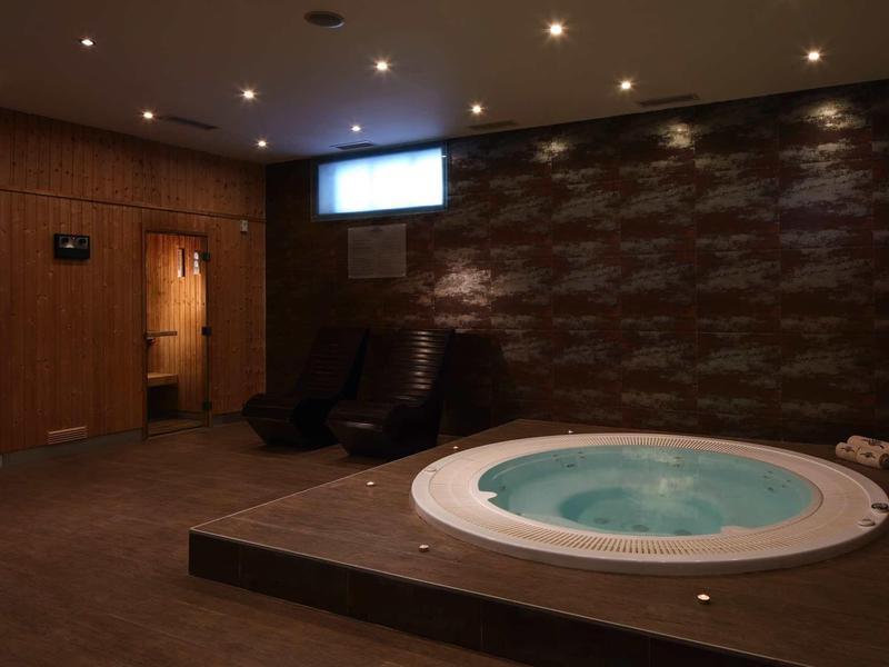 Gemütlicher Wellnessraum mit blauen Whirlpool, dunklen Holzwänden und entspannenden Sesseln.