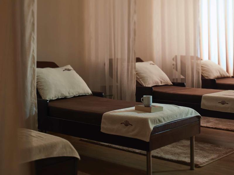 Dunkelbraune Liegen mit weißen Handtüchern und Kissen in einem schwach beleuchteten Raum.