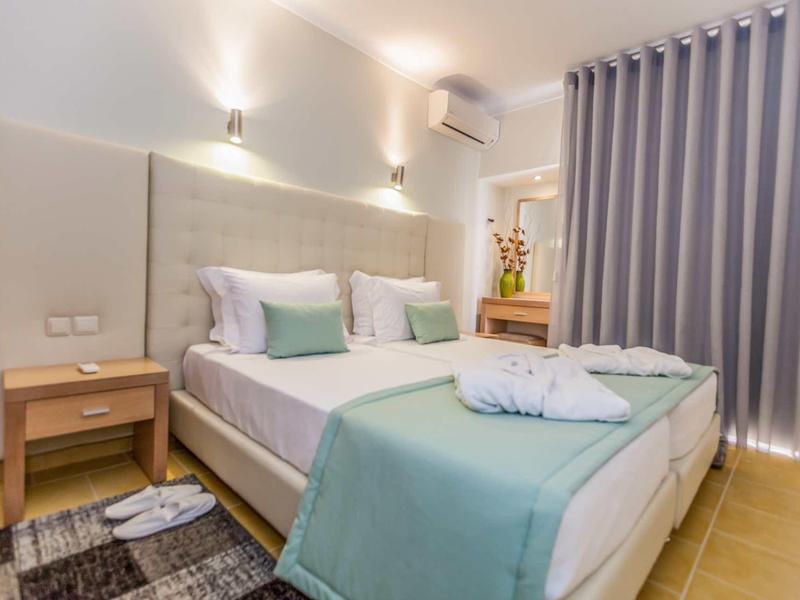 Gemütliches Schlafzimmer mit Doppelbett, hellen Wänden, Holz-Nachttisch und grauen Vorhängen.