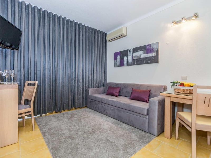 Moderner Wohnraum mit grauem Sofa, Teppich, Holzmöbeln, Fernseher und grauen Vorhängen.