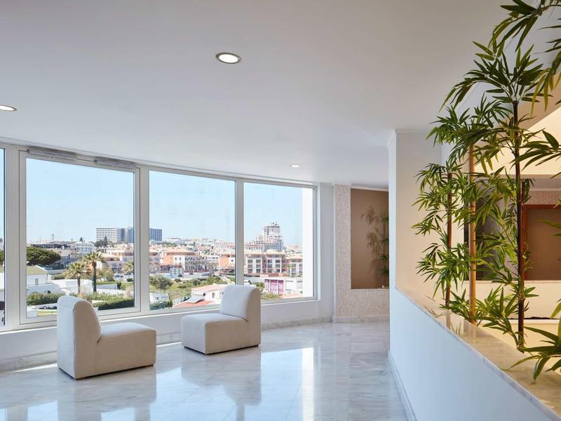 Moderner heller Raum mit großen Fenstern, zwei weißen Sesseln und grünen Pflanzen auf der rechten Seite.