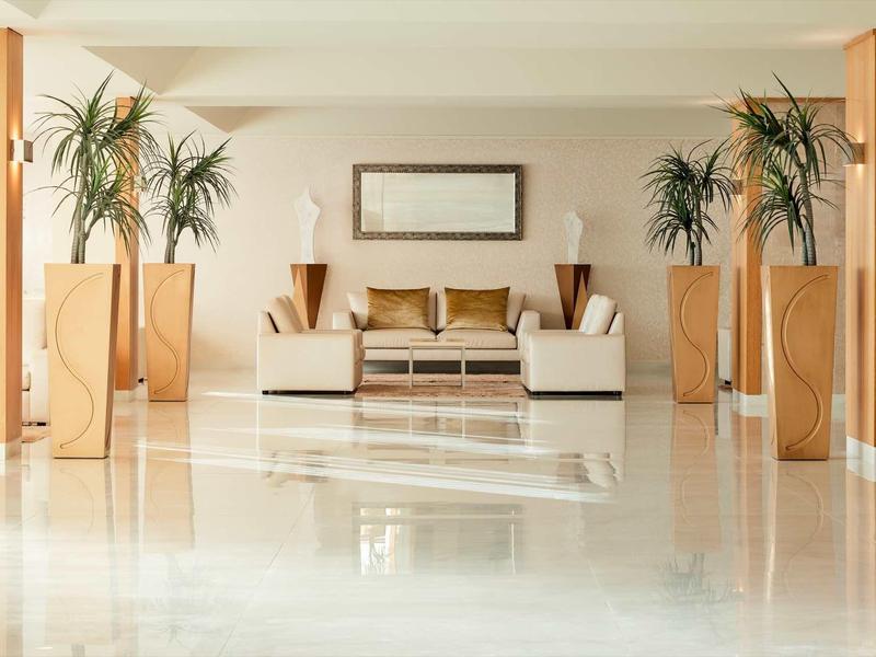 Heller Raum mit glänzendem Marmorfußboden, Sofa, Couchtisch und hohen Zimmerpflanzen.