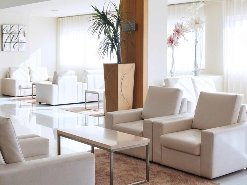 Helles Wohnzimmer mit weißen Sesseln, Glasfenstern, großem Pflanze und modernem Holztisch.