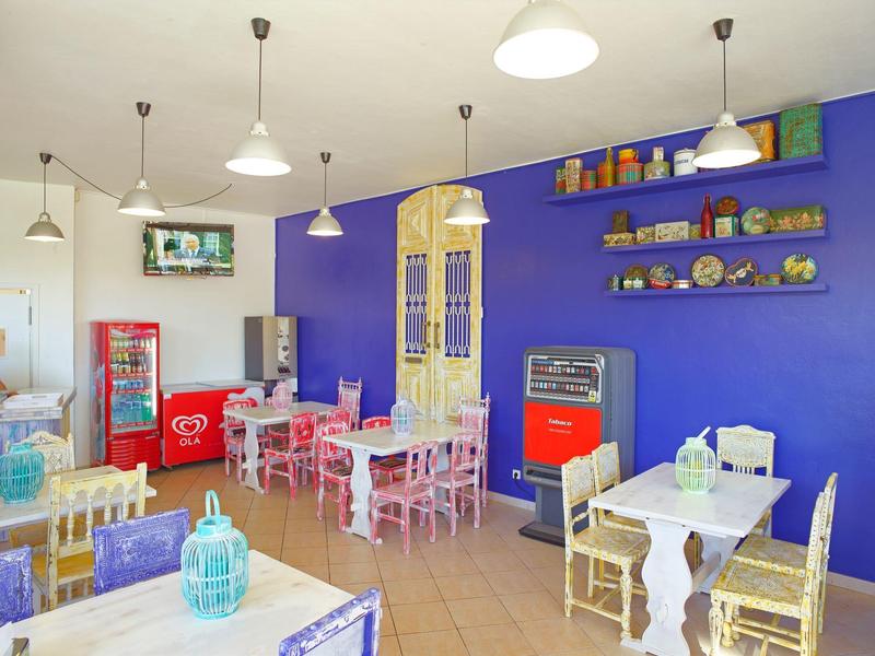 Buntes Café mit lila Wand, weißen und roten Möbeln, Pflanzen und Dekoration auf Regalen.