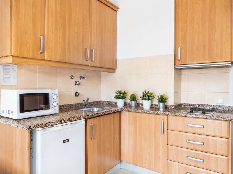 Kleine Küche mit hellen Holzschränken, grauer Arbeitsplatte, Mini-Kühlschrank und Topfpflanzen.