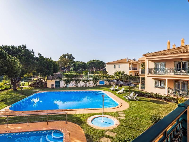 Wohnanlage mit blauem Pool, Liegestühlen, grünen Bäumen und klarem Himmel am Nachmittag.