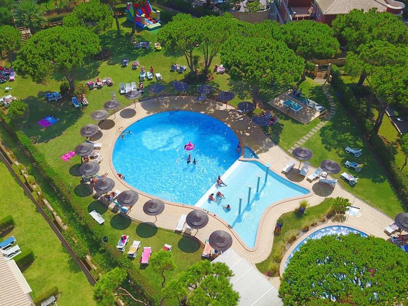 Rundlicher Pool mit blauen Liegen, Sonnenschirmen und grünen Bäumen im umliegenden Garten.