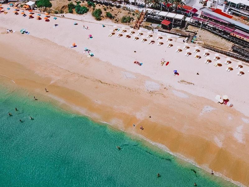 Breiter Sandstrand mit bunten Sonnenschirmen und türkisblauem Meer an einer Küstenstadt.