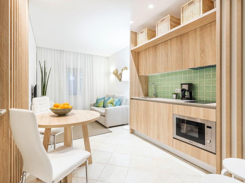 Modernes Wohnzimmer mit hellen Holzmöbeln, grünem Fliesenspiegel und weißem Essbereich.