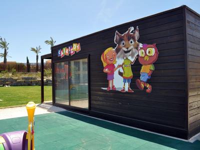 Schwarzes Holzgebäude mit buntem Cartoon-Wandbild auf grünem Boden und blauem Himmel.