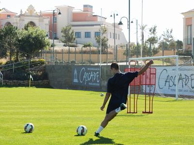 Fußballspieler trainiert Schüsse auf dem grünen Spielfeld mit Torwarttraining-Ausrüstung.
