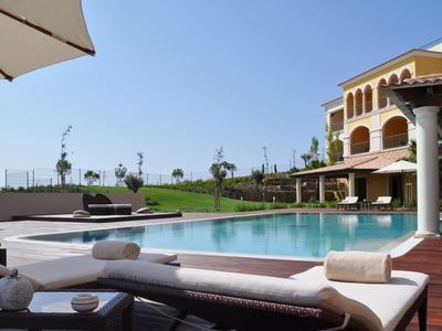 Luxuriöser Poolbereich mit Sonnenliegen und Sonnenschirm neben einem Hotelgebäude bei klarem Himmel