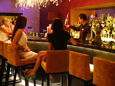 Bar mit warmem Licht, Menschen sitzen auf hohen Stühlen, Barkeeper mixt Getränke am Tresen.