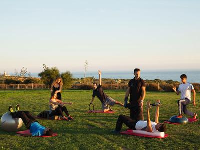 Menschen praktizieren Yoga auf einer Wiese mit Meerblick bei Sonnenuntergang.