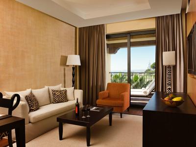 Helles Wohnzimmer mit beiger Wand, weißem Sofa, orangem Sessel und Blick auf Balkon und Garten.