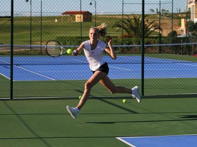 Eine Frau in sportlicher Kleidung springt auf einem Tenniscourt mit Schläger in der Hand.