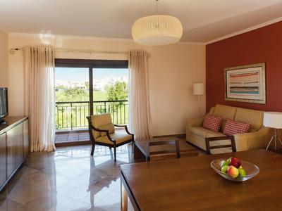 Helles Wohnzimmer mit Sofa, Fernseher, Holztisch und Balkon mit grüner Aussicht.