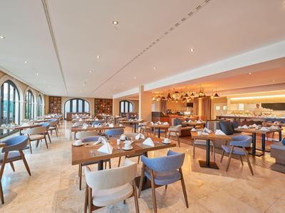 Großes modernes Restaurant mit Holztischen, blauen und weißen Stühlen und großen Rundbogenfenstern.