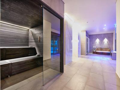 Moderner Wellnessbereich mit Sauna und gemütlicher Lounge, helle Fliesen und dezente Beleuchtung.