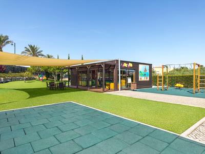 Spielplatz mit weichem Boden, Klettergerüst, Sonnenschutz und moderner Hütte in sonniger Umgebung.